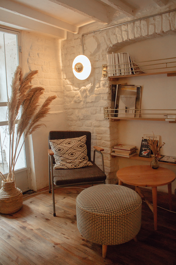 murs-blancs-coin-lecture-cocooning-lumiere-tamisée lumière tamisée dans un salon blanc cocooning, table basse bois, chaise grise, tabouret noir et blanc