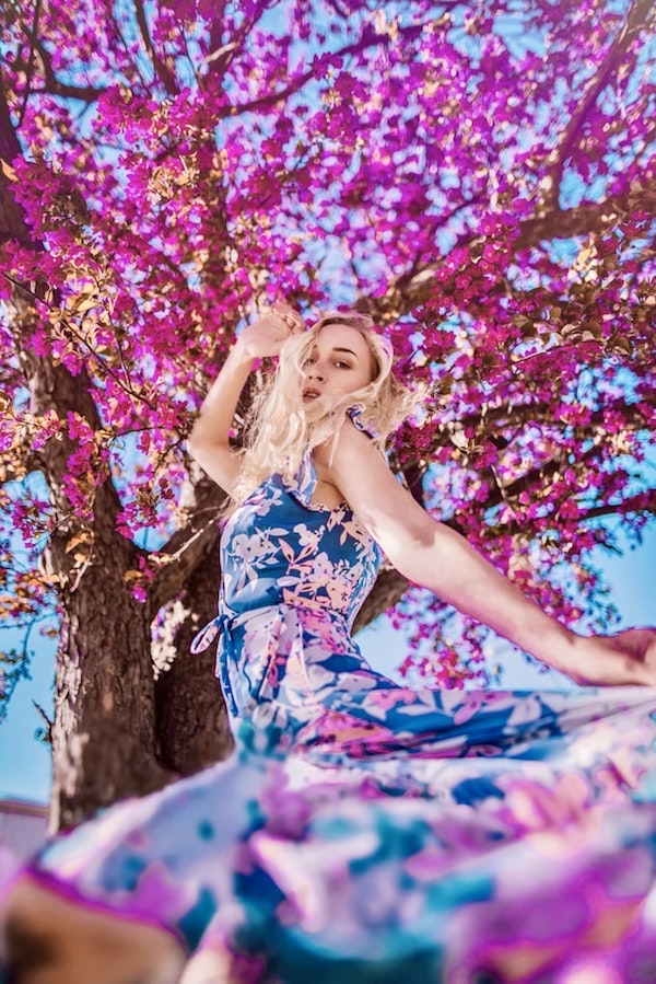 robe fleurie longue de couleur bleue avec des fleurs rose éparpillées, femme dessous un arbre aux fleurs fuchsia